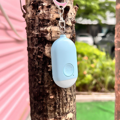 Small blue oval shaped device featuring a keychain and SOS emergency button hanging off a tree outdoors. - The Spy Store