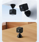 Two black cube-shaped cameras with cone bases, one mounted on a ceiling and one placed on a wooden table.