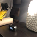 1080P HD Wi-Fi Camera Clock positioned on bedside table with items for size comparison, second view.