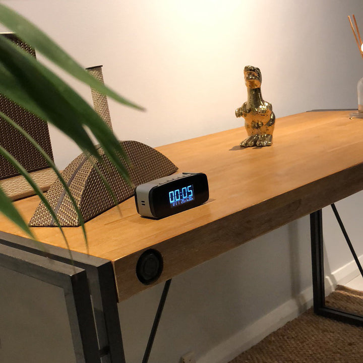 1080P HD Wi-Fi Camera Clock positioned atop a wooden desk with items for size comparison.